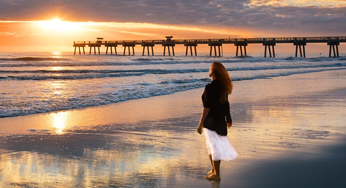 Frau steht am Strand und blickt aufs Meer
