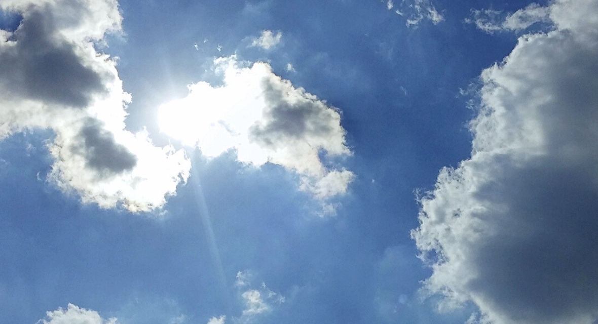 Sonne strahlt hinter einer Wolke am blauen Himmel